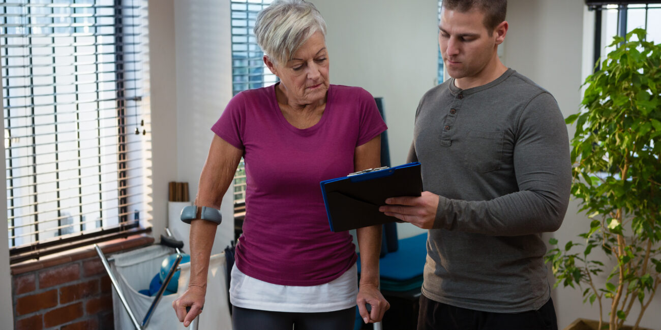 Physiotherapist discussing medical report on clipboard with senior woman in clinic