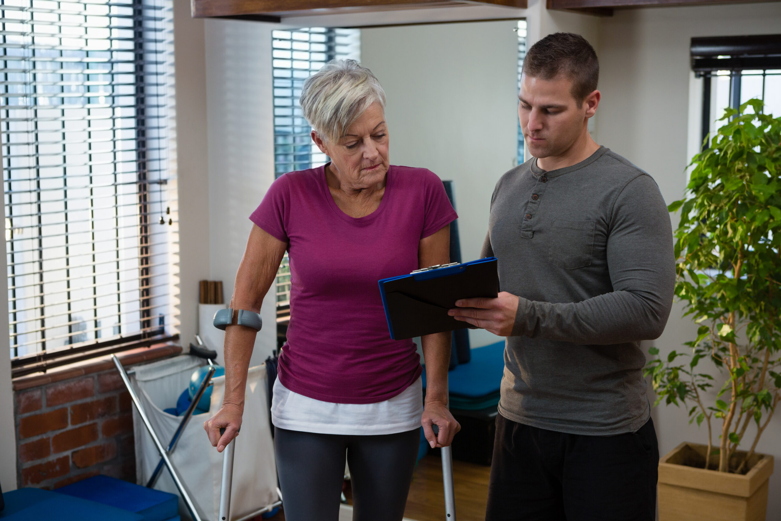 Physiotherapist discussing medical report on clipboard with senior woman in clinic
