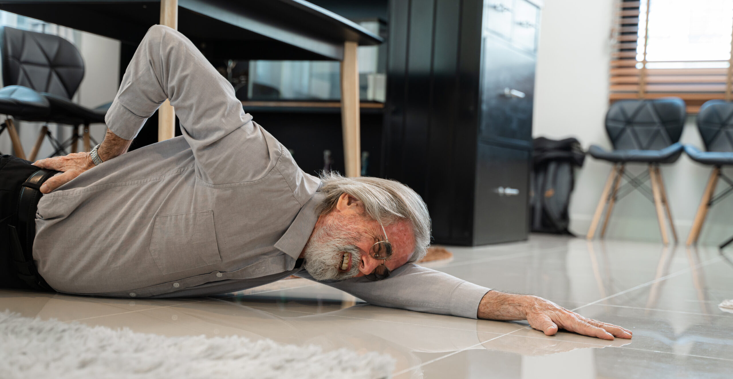 Senior man suffering from back pain after falling on floor in an office