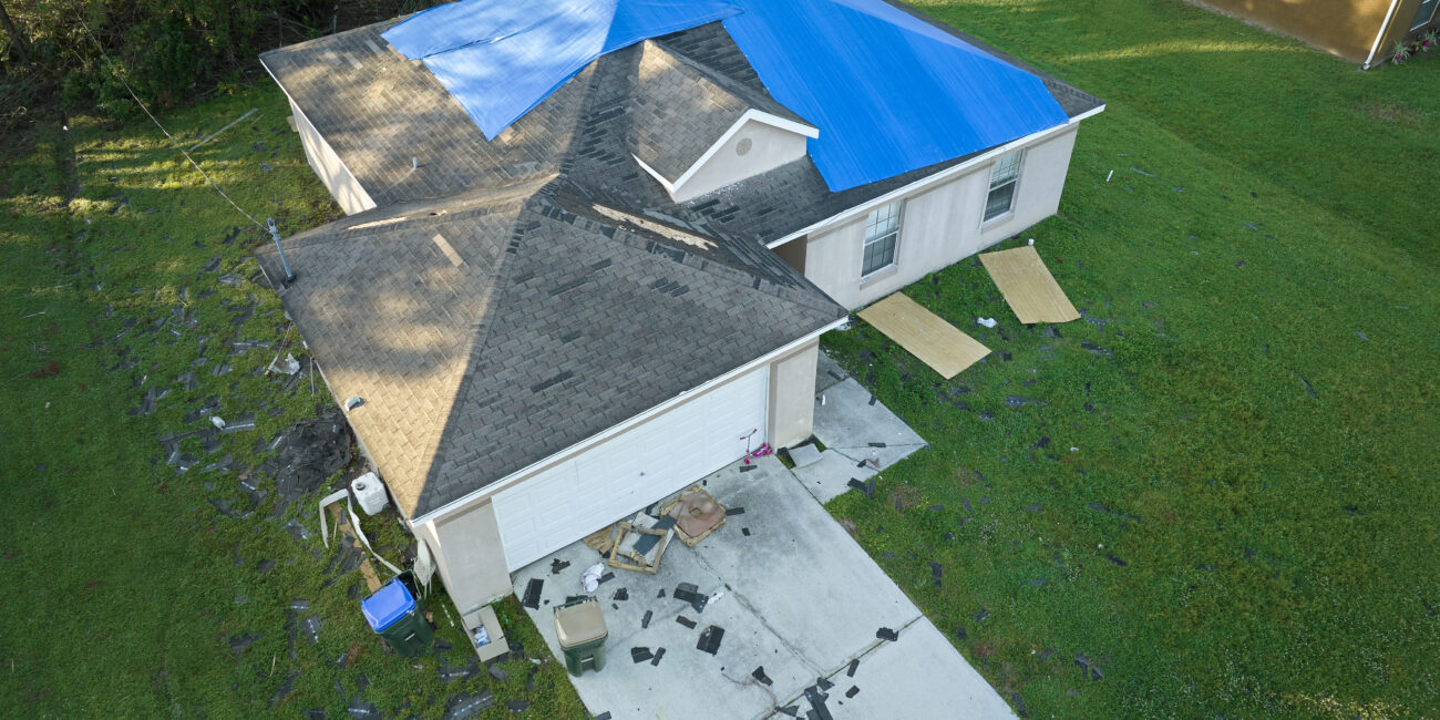 Top view of leaking house roof covered with protective tarp sheets against rain water leaks until replacement of asphalt shingles. Damage of building rooftop as aftermath of hurricane